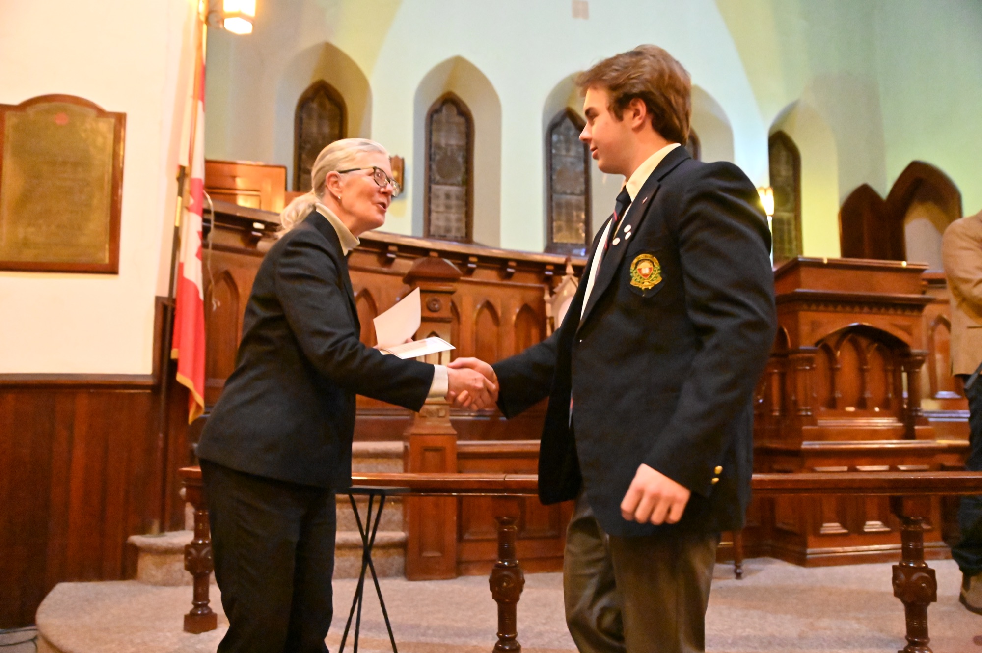 A confident student shakes hands as he is congratulated at a school ceremony